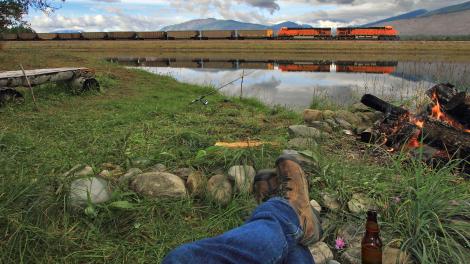 モンタナ州フロッグポンドを列車が通過するのを眺めながら、キャンプファイヤーの前でリラックス